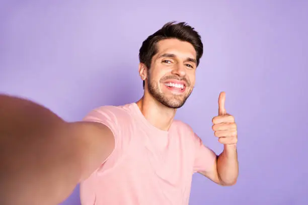 Self-portrait of his he nice attractive confident cheerful cheery glad bearded, brunet guy wearing pink tshirt showing thumbup ad advert advice isolated on violet purple lilac pastel color background
