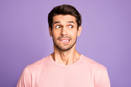 Close-up portrait of his he nice attractive funny confused brunet bearded guy wearing, pink tshirt waiting news biting lip isolated over violet purple lilac pastel color background