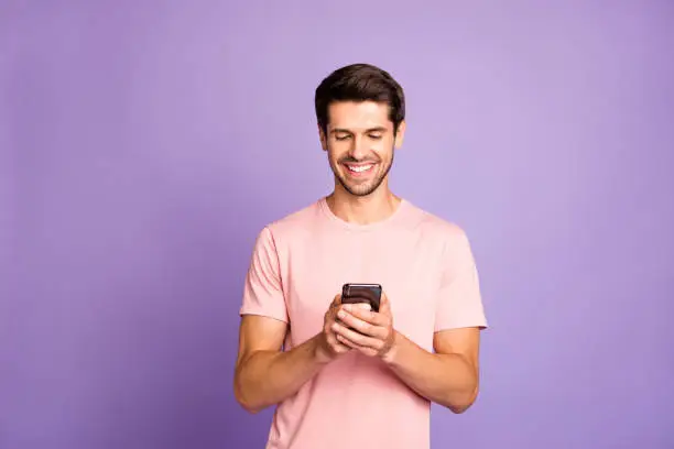 Photo of Portrait of his he nice attractive cheerful cheery guy wearing pink tshirt holding in hands using 5g app cell modern technology isolated over violet purple lilac pastel color background
