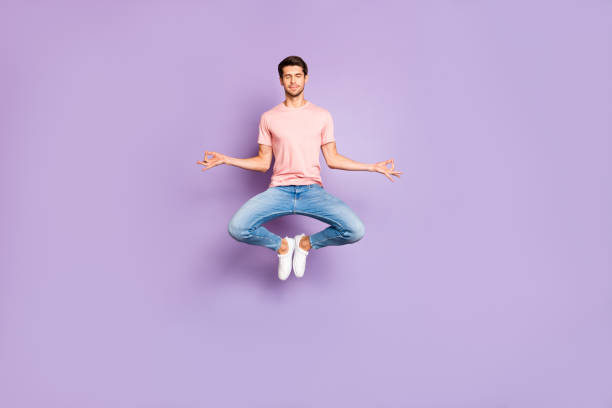 Full length photo of amazing guy jumping in yoga practice exercises closing eyes wear casual outfit isolated on purple color background Full length photo of amazing guy jumping in yoga practice exercises, closing eyes wear casual outfit isolated on purple color background cross legged photos stock pictures, royalty-free photos & images