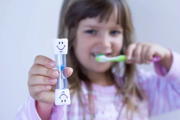 Child measures time with hourglass while brushes teeth. Healthy habits, dentalcare concept. Close up.