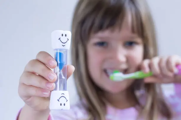 Child measures time with hourglass while brushes teeth. Healthy habits, dentalcare concept. Close up.