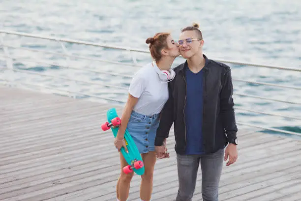 Photo of Youth summer time. Stylish hipster couple in love strolling and kissing along the beach promenade.