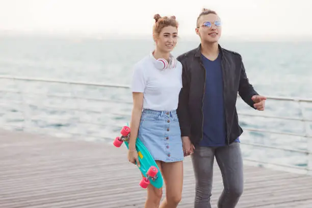 Photo of Youth summer time. Stylish hipster couple in love strolling along the beach promenade.