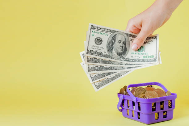 istock Shopping basket with coins and dollar bills in hands on yellow background. Space for text. Close up. Business concept. 1179593314