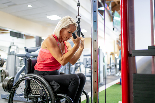 Adaptive athlete in a wheelchair working on her upper body muscles in a gym. Hawaii, USA