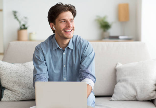istock Man In Earphones Using Laptop Sitting On Couch At Home 1179597529