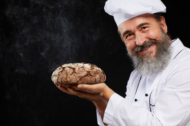 bearded baker holding fresh bread against black - baking traditional culture studio shot horizontal imagens e fotografias de stock