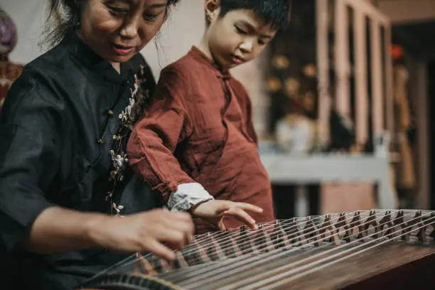 Chinese grandmother and grandson in traditional clothes playing harp