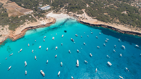 Many boats over turquoise sea and small cliff. Cala Saona in Formentera island.