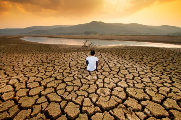 Climate change and Drought Climate change and global warming concept. Children sitting on drying lake with the sky turning orange by an pollution from industrial or city. drought stock pictures, royalty-free photos & images