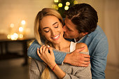 Tender moment. Man kissing wife in front of Christmas tree