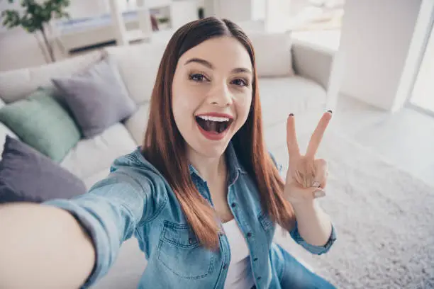 Hello everyone. Close up photo of funky positive cheerful girl have, journey sit at house indoors take selfie make v-signs enjoy recreation wear denim jeans outfit