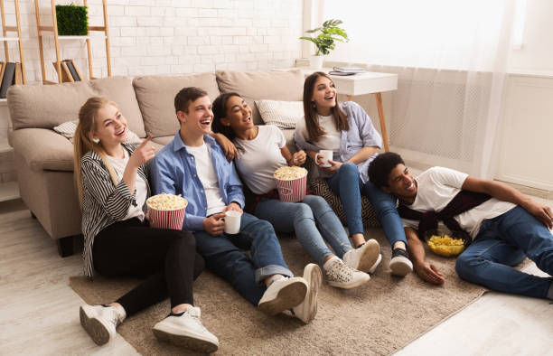 счастливые друзья смотрят комедийный фильм и едят попкорн - movies at home стоковые фото и изображения