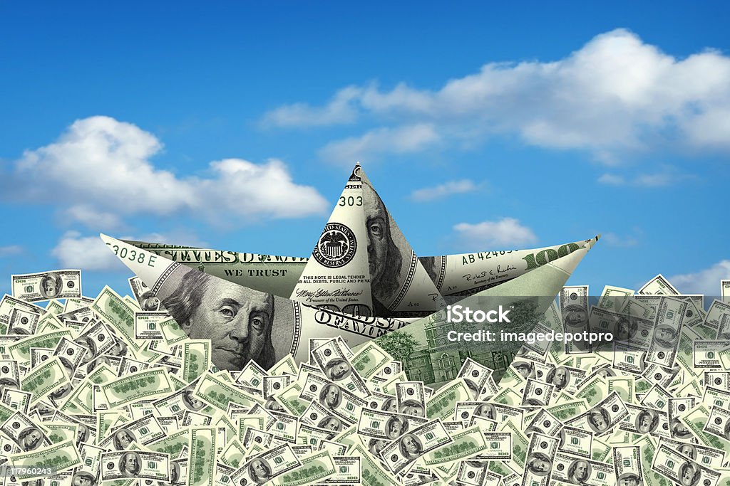 dollar ship money boat swimming on 100 dollar bills over cloudy sky. US Paper Currency Stock Photo