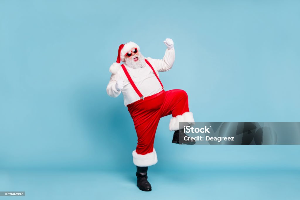 Full body photo of crazy funny funky fat santa with big belly raise fists scream yeah enjoy christmas party wear red pants style stylish boots overalls spectacles isolated over blue color background Full body photo of crazy funny funky fat santa with big belly raise fists scream, yeah enjoy christmas party wear red pants style stylish boots overalls spectacles isolated over blue color background Santa Claus Stock Photo