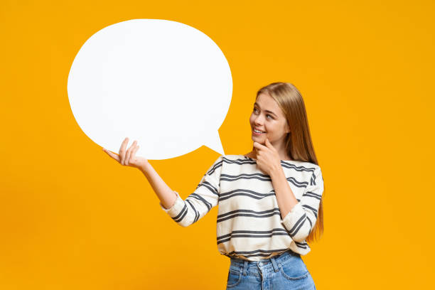 Pensive young girl holding blank speech bubble over yellow background