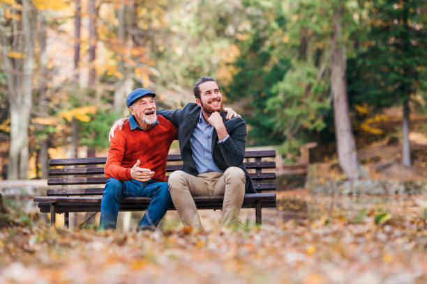 Senior father and his son sitting on bench by lake in nature, talking. Senior father and his young son sitting on bench by lake in nature, talking. sitting on bench stock pictures, royalty-free photos & images