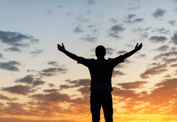 istock Man with arms outstretched standing on a cliff at sunset 1179604086
