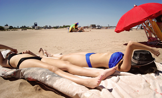 two girls is getting tan on the lying in the sun at beach of Mar del Plata. They are covering their faces from sun.