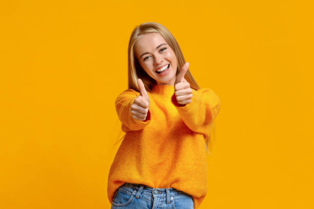 オレンジ色の背景に親指を示す喜びの十代の少女 - thumbs up child success winning ストックフォトと画像