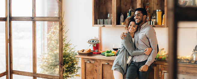 Happy millennial black man and woman embracing at kitchen, looking aside, panorama, copy space