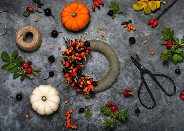 Photo of Making autumn wreath on dark florist table with colorful wild rose hips and firethorn berries.
