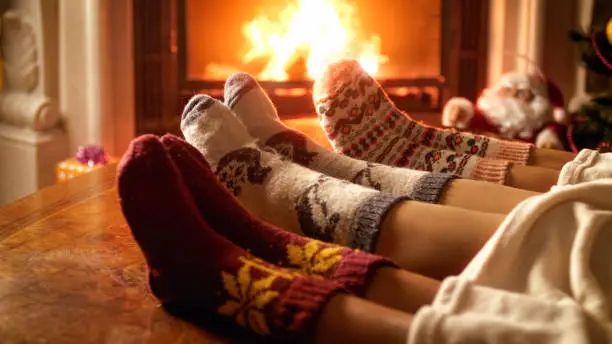 Photo of Closeup photo of family feet in woolen socks lying next to fireplace