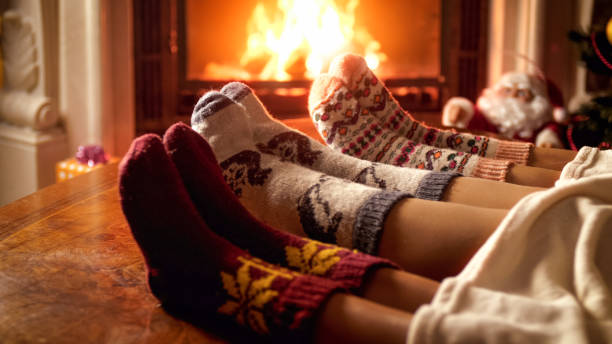 famille dans les chaussettes tricotées chaudes se trouvant sur le sofa à côté de la cheminée brûlante - blanket fireplace winter women photos et images de collection