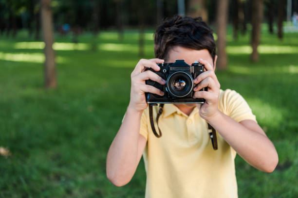 istock cute boy holding digital camera while talking photo in park 1179612553