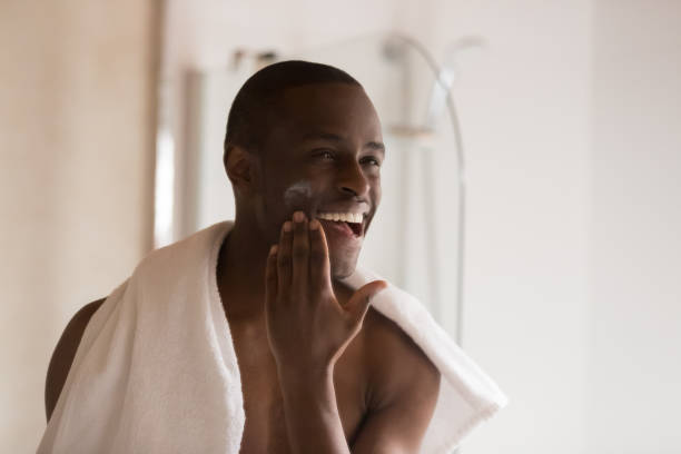 istock Happy smiling african ethnicity man applying moisturizing balm on cheek. 1179614257