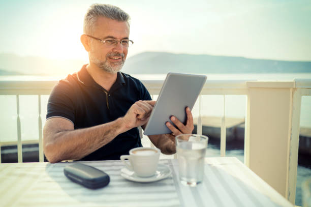 homme s'asseyant à un café et utilisant la tablette numérique - reading beach e reader men photos et images de collection