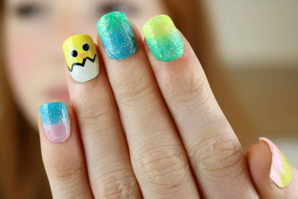 Image of red haired teenage girl 14 / 15 holding up fingernails painted with Easter chick springtime design, yellow, blue and pink and black nail varnish, focus on foreground Stock photo of ginger haired teenager modelling nail varnish painted with the design of a springtime Easter chick. yellow nail polish stock pictures, royalty-free photos & images