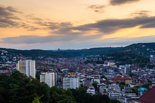 Germany, Beautiful orange sunset sky over houses of swabian big city stuttgart in basin surrounded by forested hills, aerial view from above