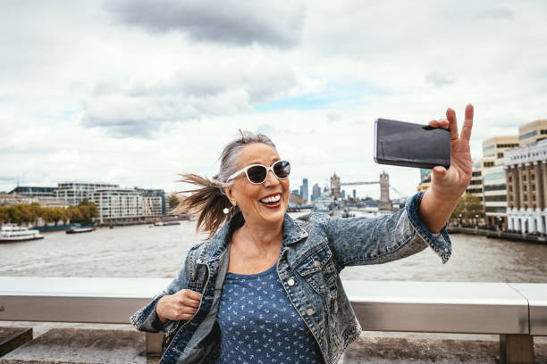 senior tourist in london taking selfie with tower bridge in background - tower bridge fotos imagens e fotografias de stock
