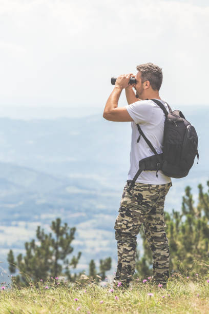 istock Traveler with backpack standing on the top of the mountain and using binoculars 1179625975