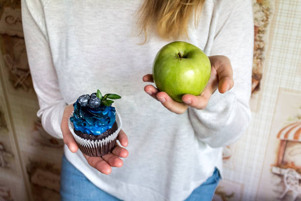 healthy eating and lifestyle green apple and sugar cupcake in the hands, the dilemma of what to choose, the concept of healthy eating and lifestyle, the problem of diet weight loss and overweight sugar control stock pictures, royalty-free photos & images