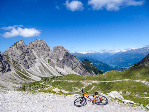 Mountain bike lying on the side of a gravelled road in tall mountain range of Lienz Dolomites, Austria. The slopes are barren with little grass on it. Dangerous mountain climbing. Clear and bright day
