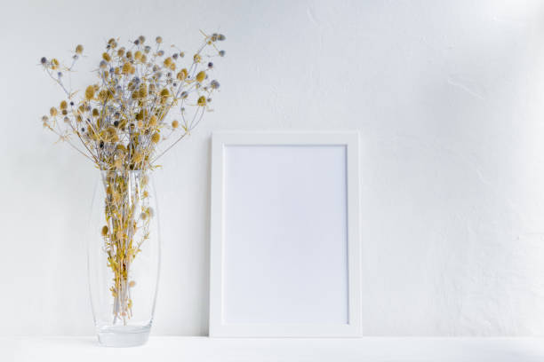 istock Mockup with a white frame and dry flowers in a vase on a white table 1179631476