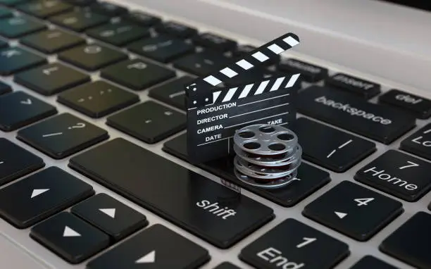 Photo of Laptop with films reel and movie clapper