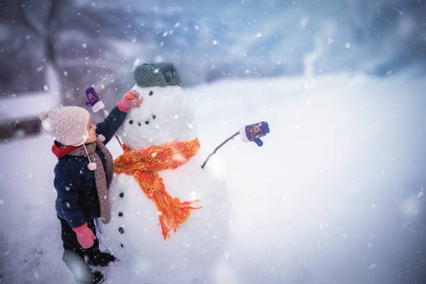 Winter outdoor activities for a child Child sculpts a snowman in a park Knitted Gloves stock pictures, royalty-free photos & images