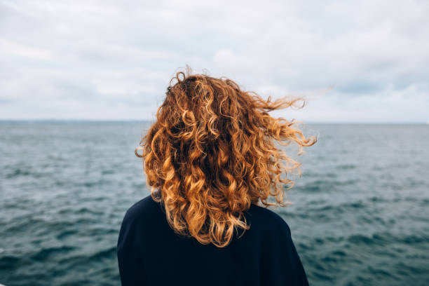 View from the back a woman with curly hair View from the back a woman with curly hair looks at the sea vista posterior stock pictures, royalty-free photos & images