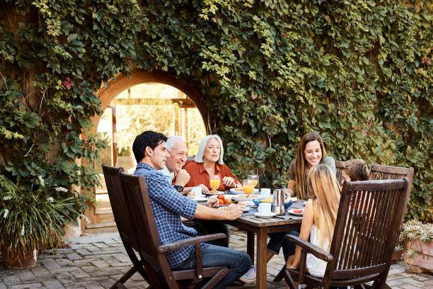 Multi-generation family having breakfast at yard Happy multi-generation family talking while enjoying food. Males and females are sitting together at dining table. They are having fun in backyard. spanish breakfast stock pictures, royalty-free photos & images