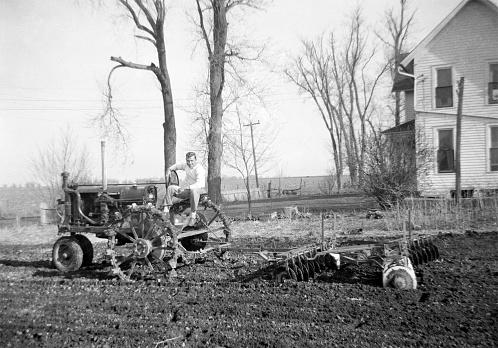 Man on tractor disking. Metal wheels on tractor. Wellman, Iowa, USA. 1941. Scanned film with grain.