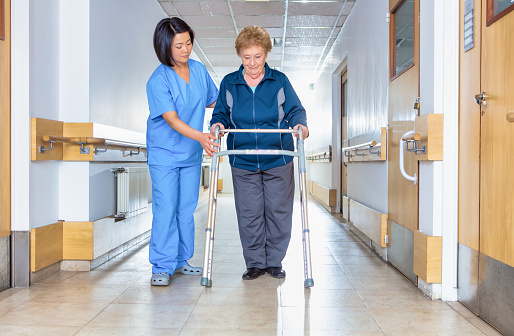 Rehabilitation Concept. Asian nurse helping elderly lady with mobility walker in rehabilitation ward.