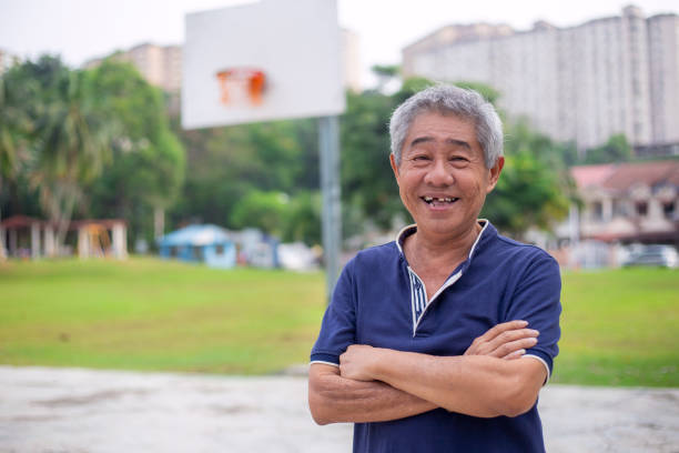 lächelnder senior asiatischer mann steht auf dem basketballplatz - senior adult exercising aging process instructor stock-fotos und bilder