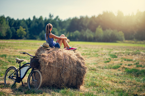 Teenage girl enjoying break during bike trip. The girl is sitting on straw bale and enjoying views.
Nikon D800