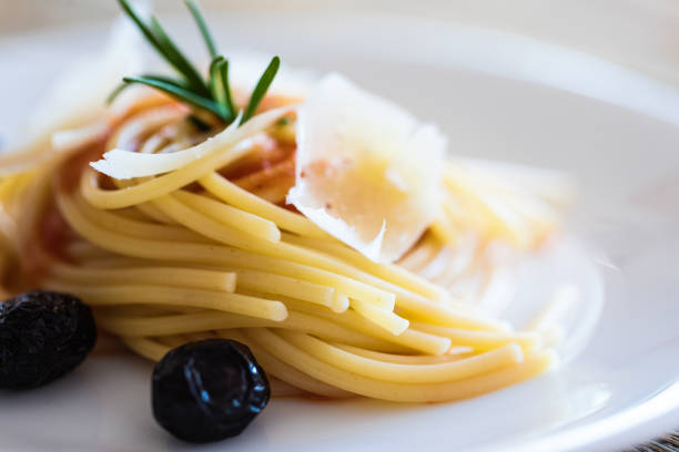 Spaghetti with tomato sauce and hard cheese with black olives on plate, close-up
