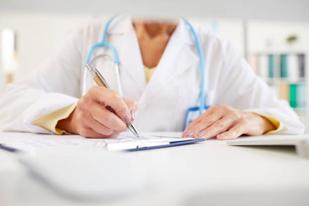 istock Close-up of unrecognizable doctor sitting at table and making notes in medical record while working with medical papers 1179655590