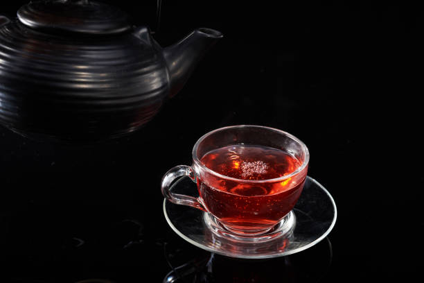 Red hot tea is poured from the teapot into a glass cup on a black background.